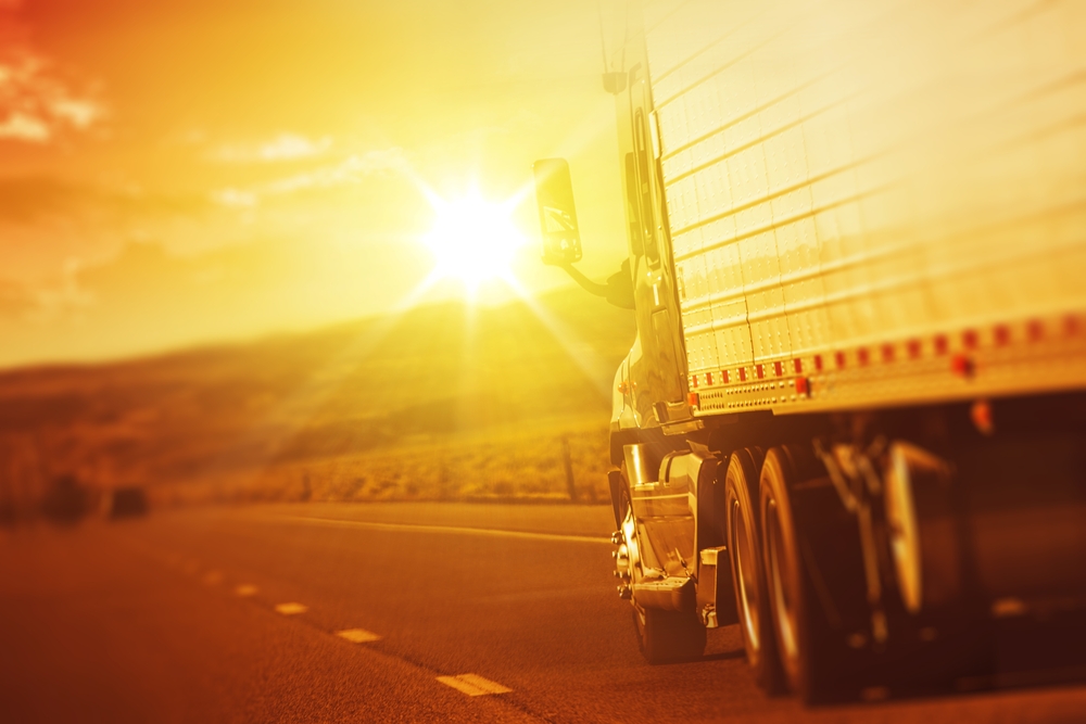 Truck driver with Alabama CDL training drives into sunset on country highway.