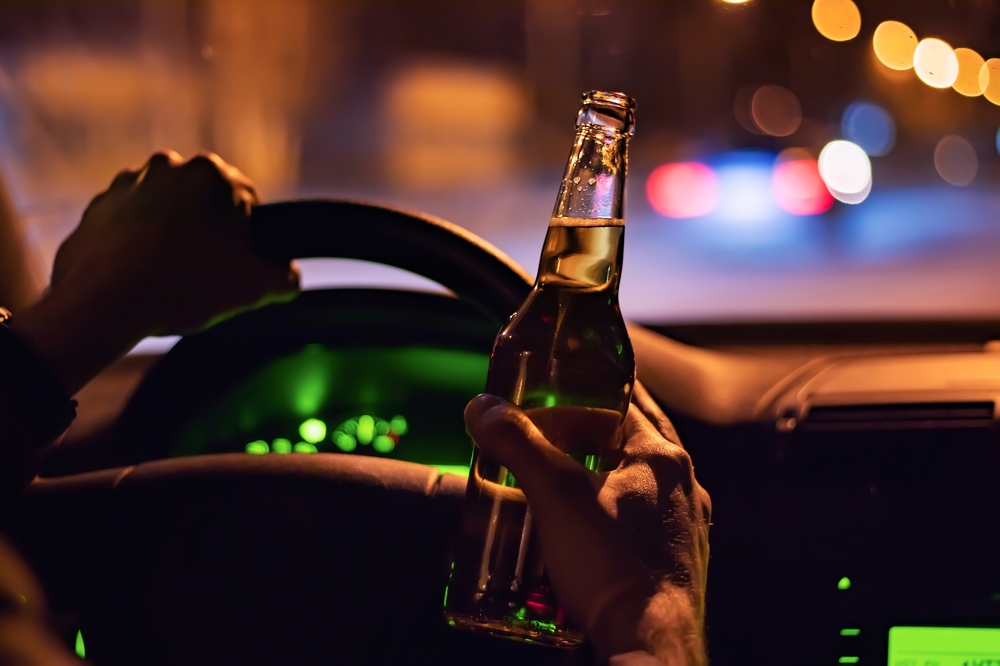 Hand holding steering wheel with other hand holding beer, showing danger of DUI accidents