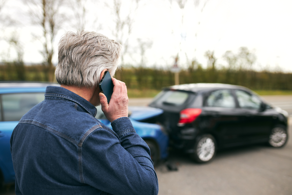 Man looking at cars after wreck is on cellphone.