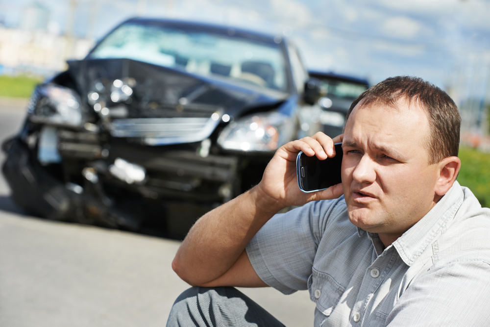 person sitting on ground in front of totaled leased car talking on cell phone